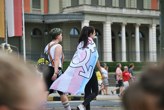 A person wearing the transgender flag as a cape