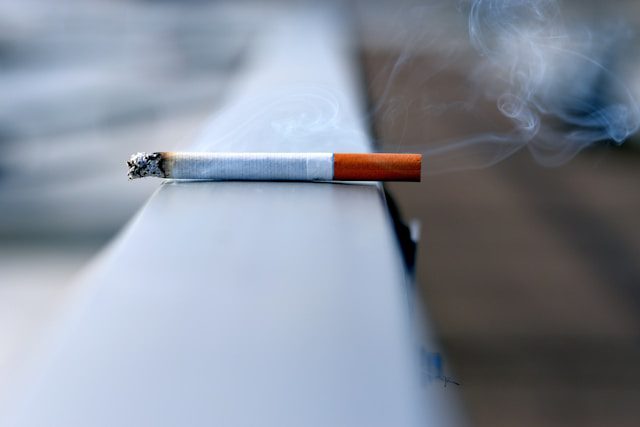 An abandoned cigarette trailing smoke while sitting on a handrail.