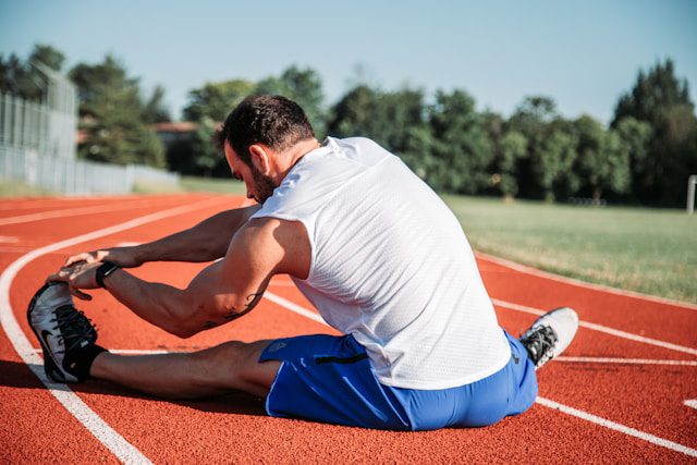 A man stretching his legs while sitting down on an outdoor track.