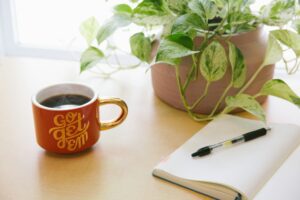 A motivational coffee mug next to a journal and a houseplant