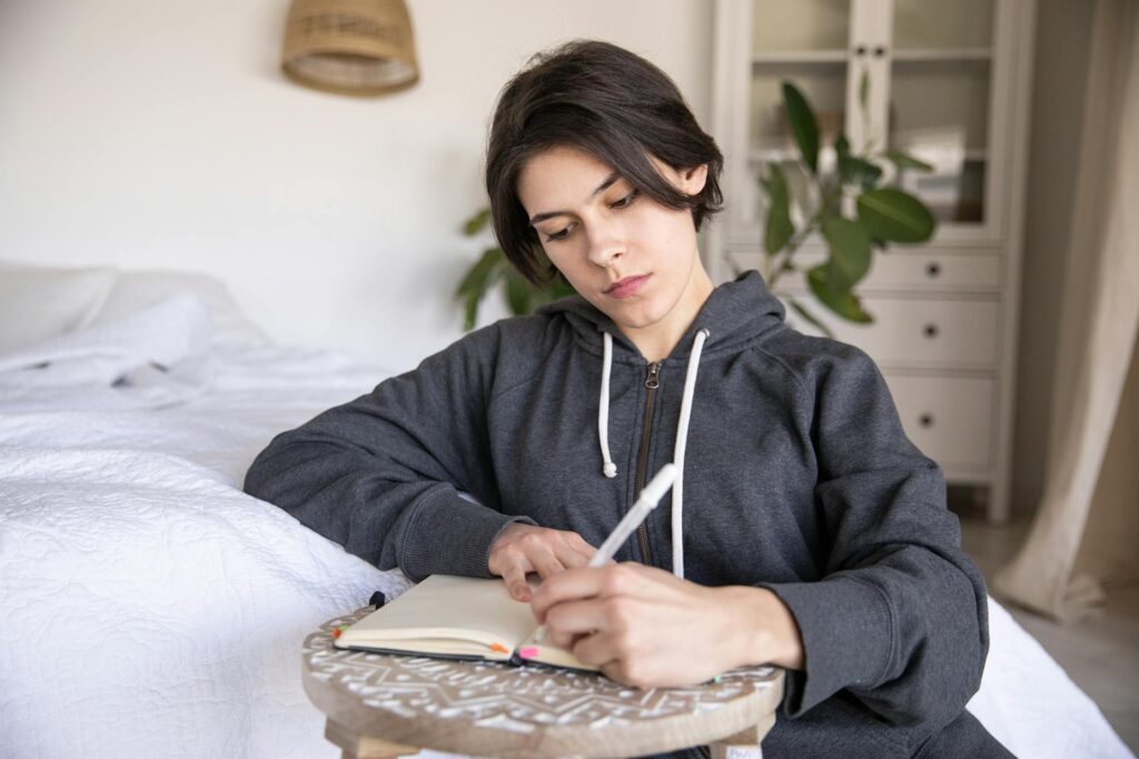 Person sitting beside a bed writing in a journal