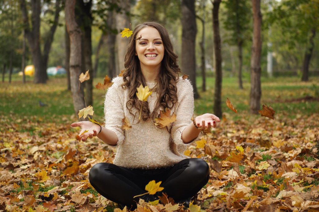 Smiling woman sitting cross legged on the ground on a pile of leaves