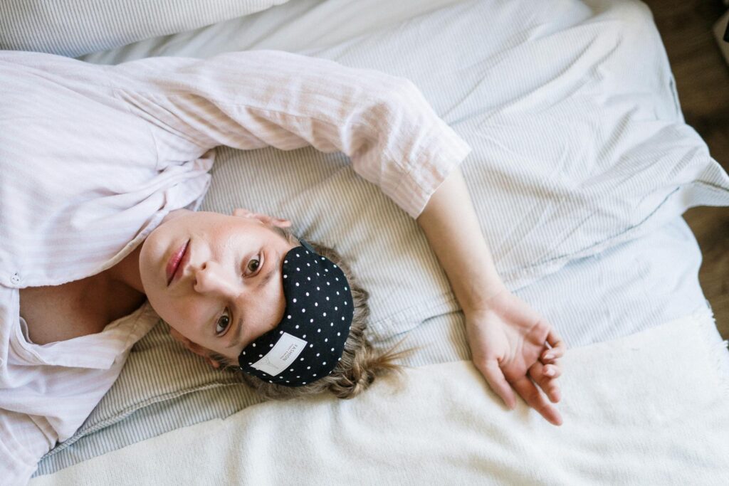 Person lying in bed with a sleep mask on their forehead looking awake 