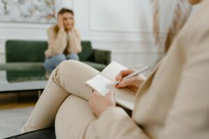 Therapist taking notes while anxious client speaks in the background