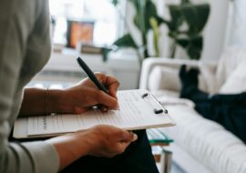 Therapist writing on a clipboard during a therapy session as a patient lies on a couch.